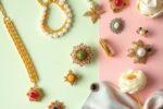 Das Bild zeigt eine elegante Flat-Lay-Komposition mit den wichtigsten Accessoire-Trends 2026: Chunky-Goldketten, moderne Perlenschmuckstücke in verschiedenen Farben, skulpturale Arm Cuffs, Statement-Ringe und Haaraccessoires – perfekt arrangiert auf pastellfarbigem Hintergrund in den Trendfarben Muted Mint und Peony Pink.