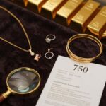 Das Bild zeigt eine luxuriöse Produktpräsentation verschiedener Goldschmuckstücke auf dunklem Samt: Eine elegante 18-Karat-Gelbgoldkette, Roségold-Ohrringe, ein Weißgold-Ring mit Diamant und gestapelte Goldarmbänder in verschiedenen Karatierungen. Im Vordergrund liegt eine Juwelierlupe neben einem Echtheitszertifikat mit sichtbarer "750"-Punzierung. Goldbarren im Hintergrund symbolisieren die Wertanlage. Die warme, professionelle Beleuchtung betont den Glanz und die Qualität des Goldes – perfekt für einen Kaufratgeber.